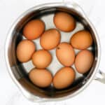 10 brown eggs in a pot with water on a marble surface
