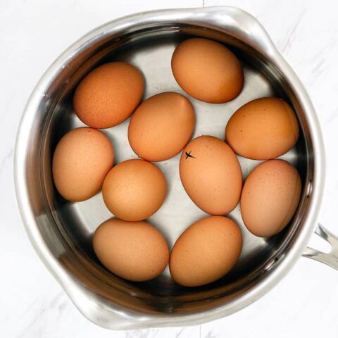 10 brown eggs in a pot with water on a marble surface