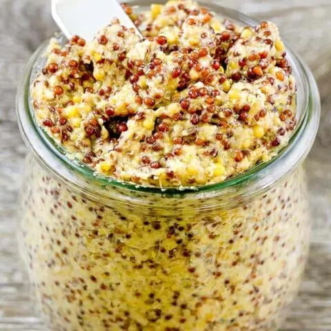 Close up of the whole grain mustard in a glass jar with a spreading knife sticking out the top