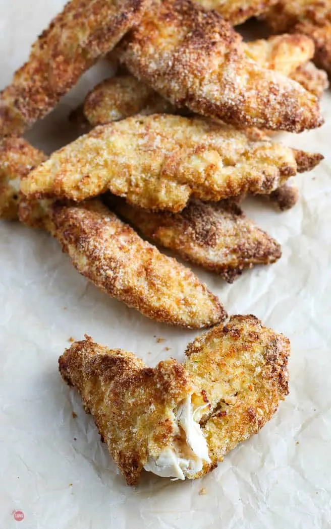 fried chicken tender torn open to see cooked meat inside on a piece of parchment paper