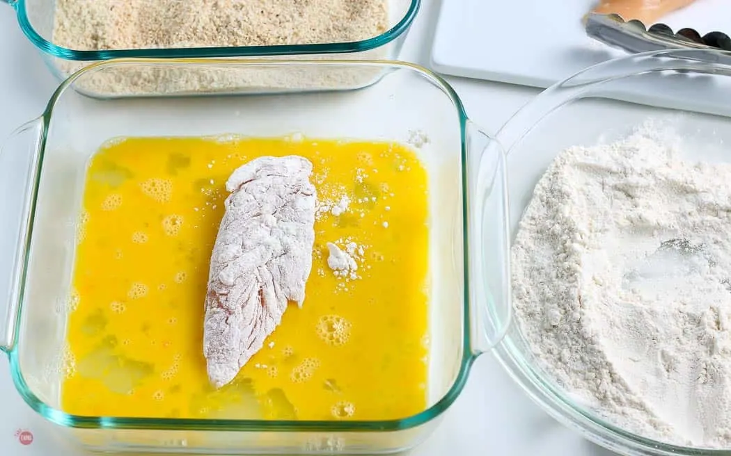 chicken tender coated in flour in a bowl of beaten egg