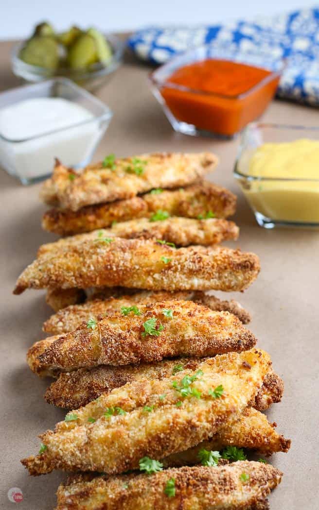 stack of chicken tenders on butcher paper with dipping sauces in the background 