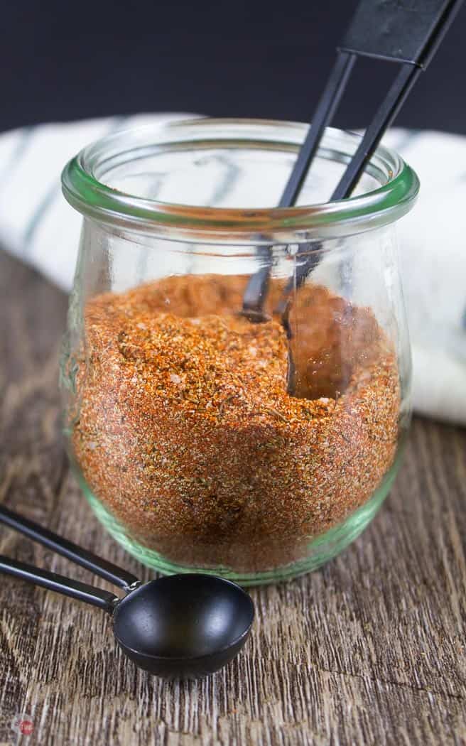 side view of clear jar with spice mix and a black measuring spoon