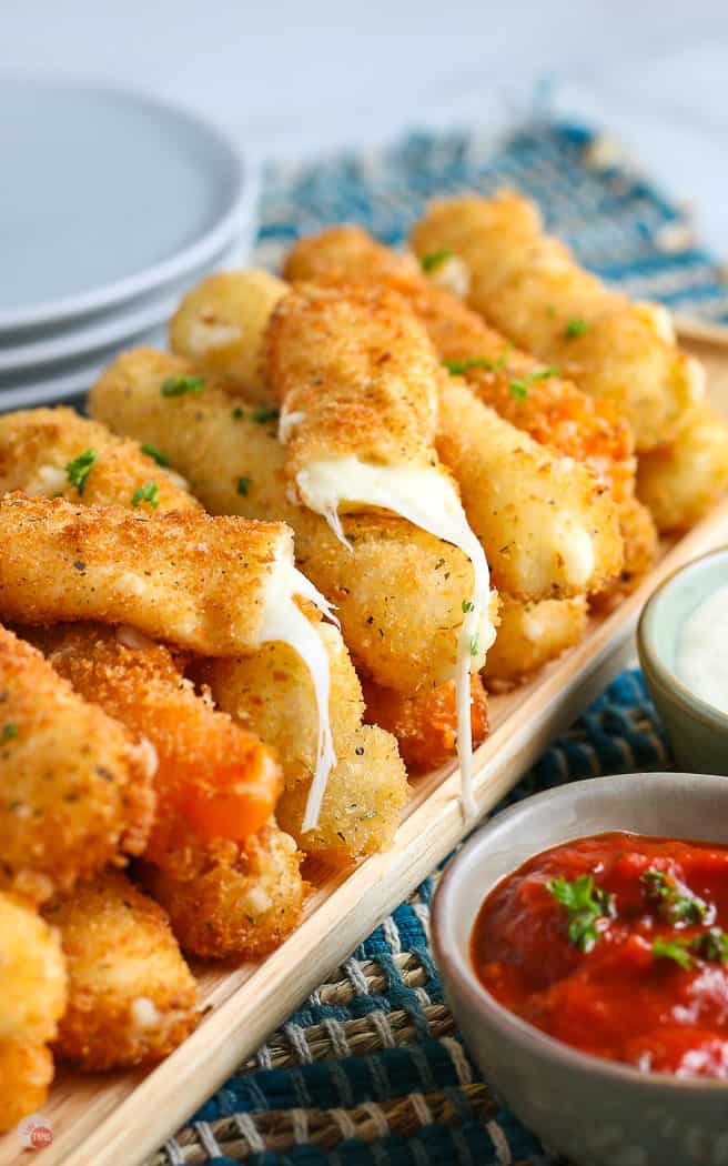 pile of cheese sticks with one broken in half and a small bowl of red sauce