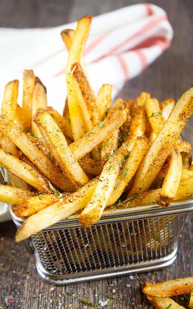 wire basket of fries with seasoning on them and a white napkin in the back