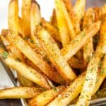wire basket of french fries with seasoning with a napkin in the back