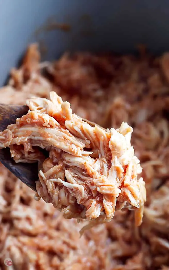 close up of pulled bbq chicken on wood spoon with crockpot in background