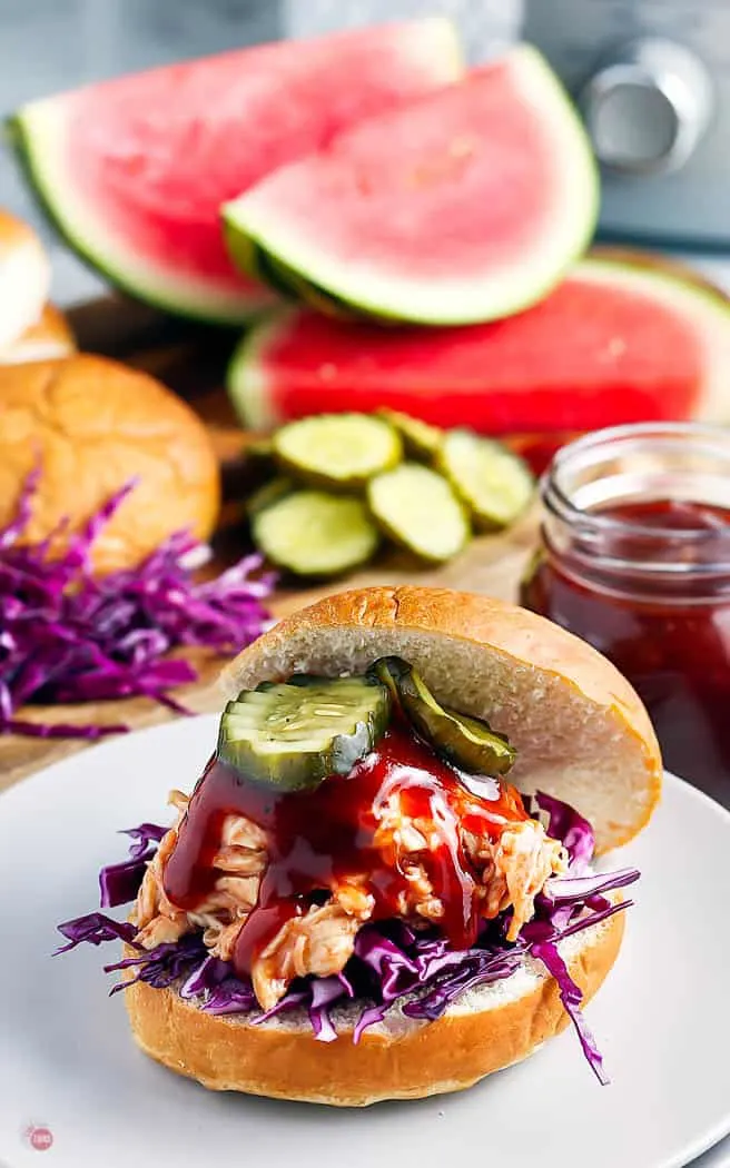 shredded chicken slider on white plate with watermelon and toppings int eh background
