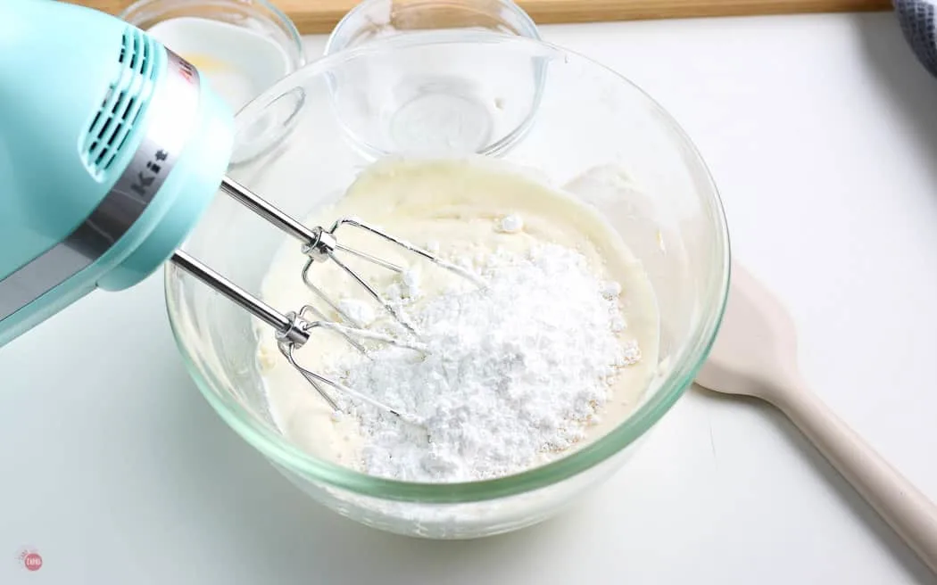powdered sugar added to cream cheese mixture in clear bowl