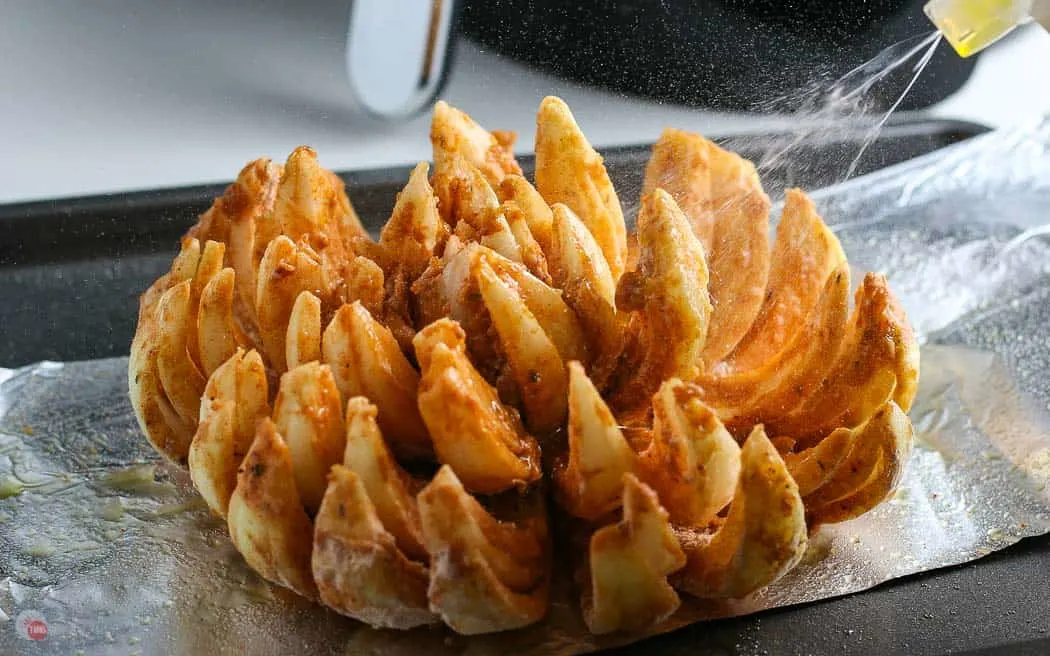 breaded onion on foil with oil being sprayed on it