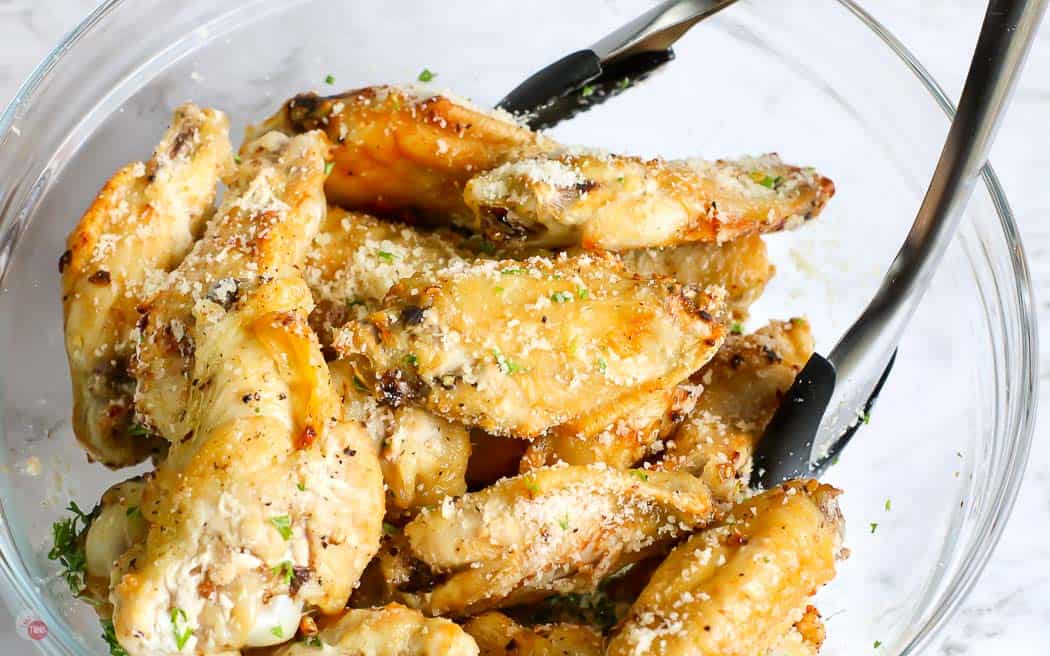 wings being tossed with tongs in a clear bowl