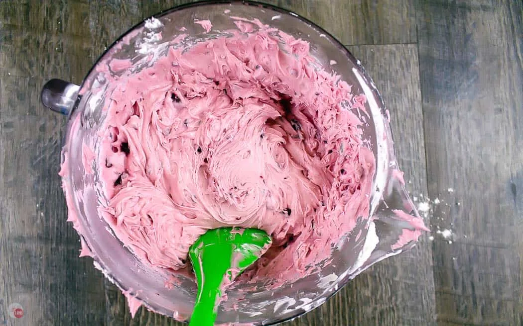 cherry frosting in a clear bowl with a green spatula