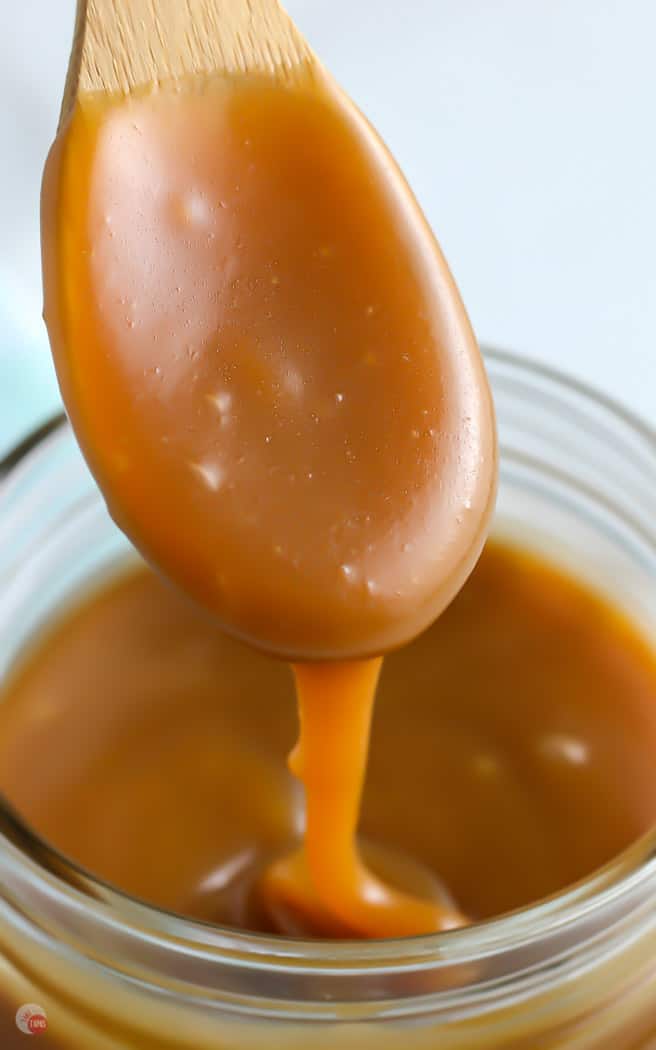 wood spoon dripping salted caramel sauce into a jar