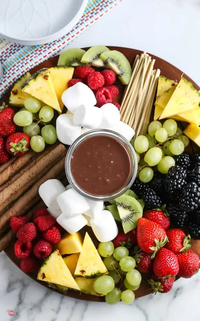 overhead picture of a wood board with chopped fruit and chocolate sauce
