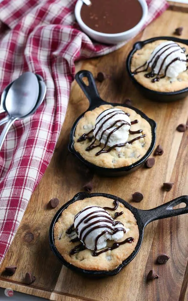 three mini cast iron skillets filled with pizookie cookies on a wood board