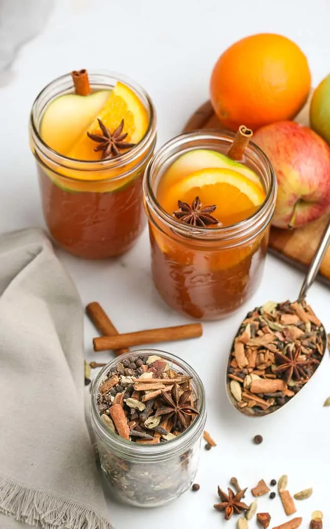 jar of fall mulling spice mix with two glasses of cider