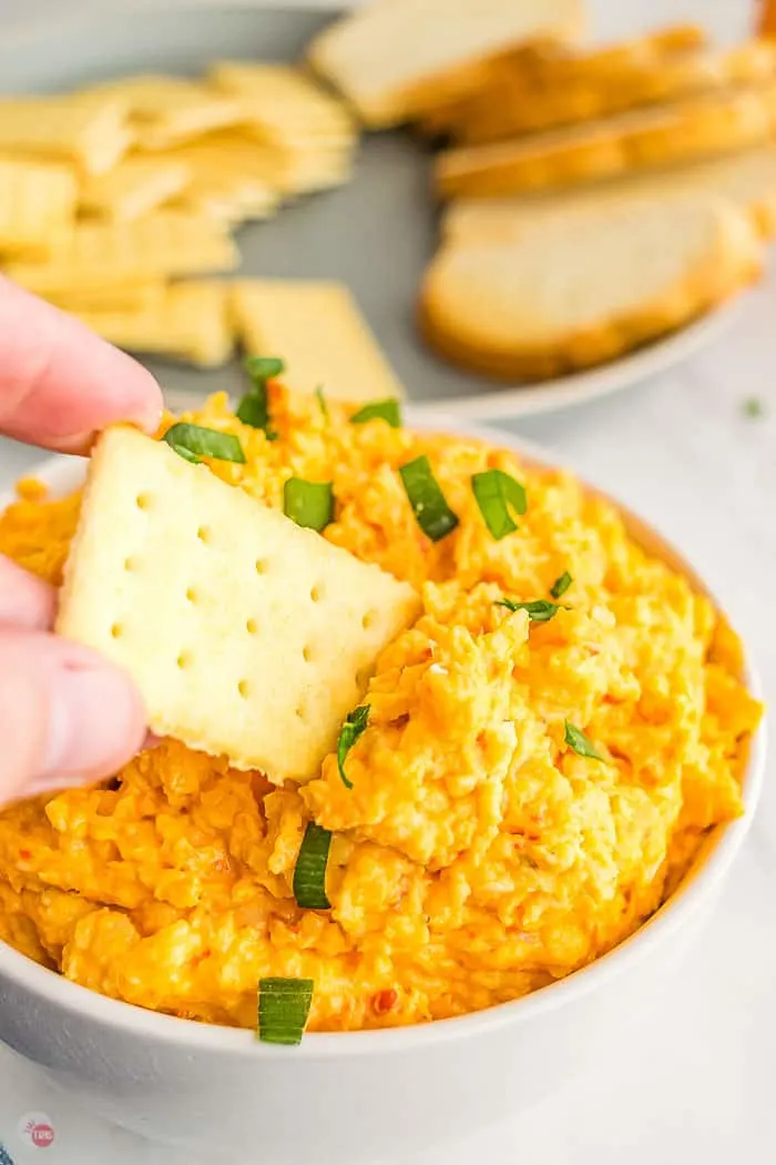 hand dipping a cracker into a bowl of pimento cheese spread