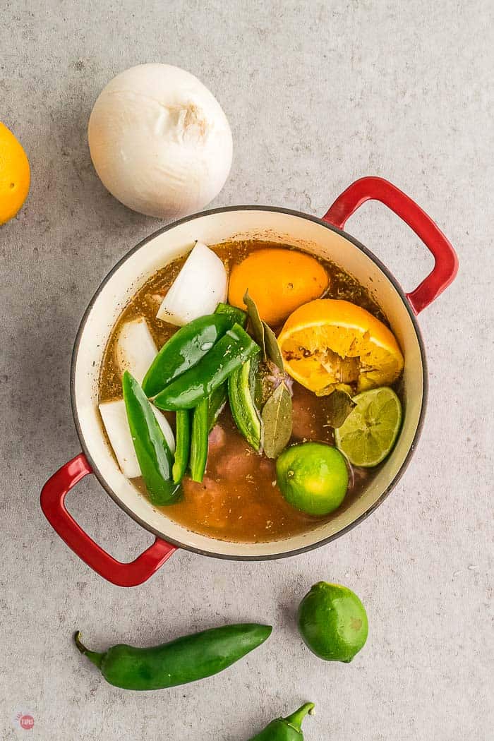 red pot with meat, water, citrus, and peppers