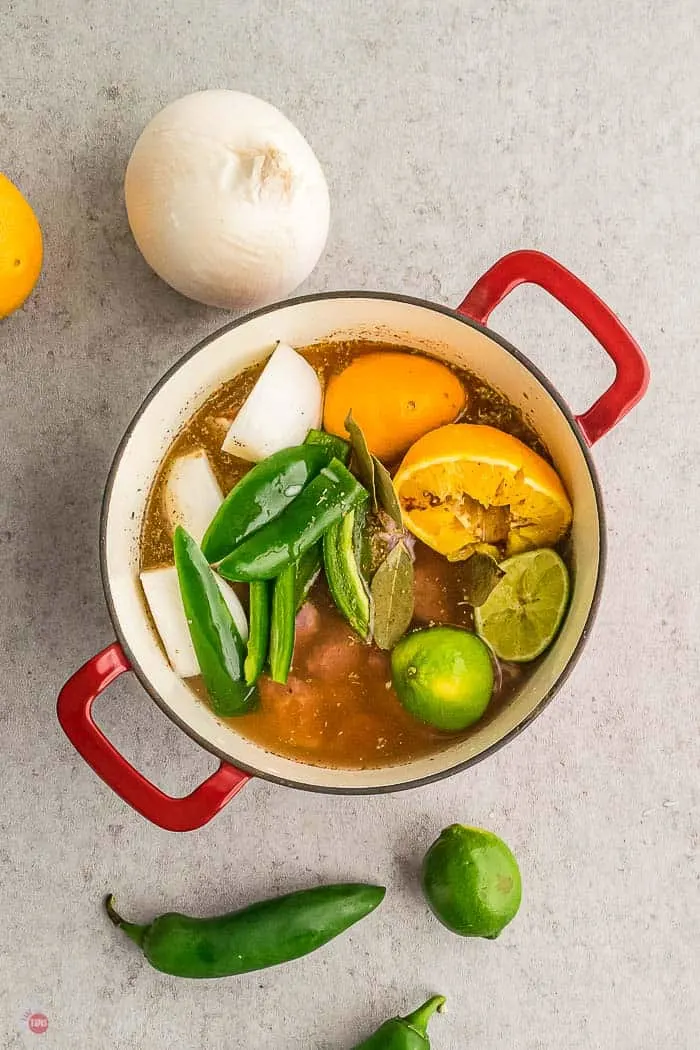 red pot with meat, water, citrus, and peppers