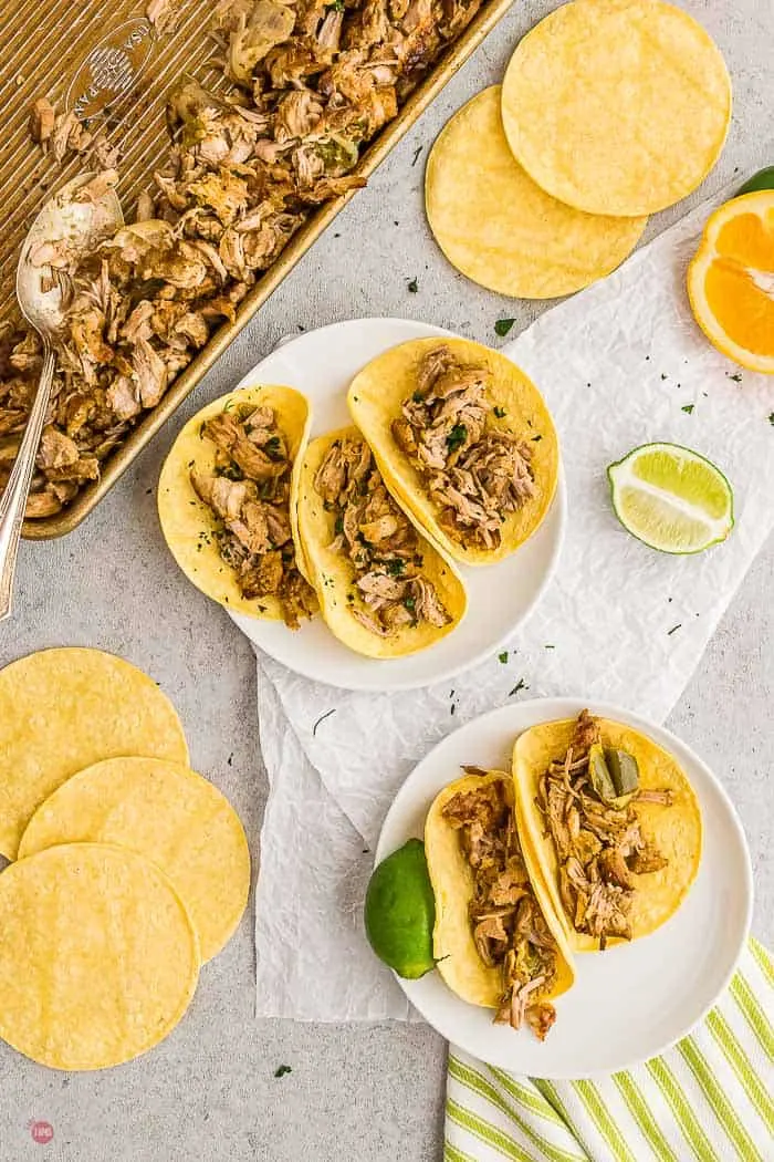 two plates of street tacos with a sheet pan of shredded pork