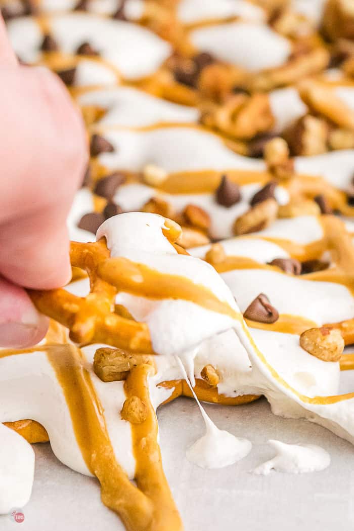 hand pulling a pretzel covered in marshmallow and peanut butter