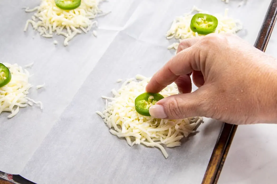 hand placing slice of jalapeno on cheese