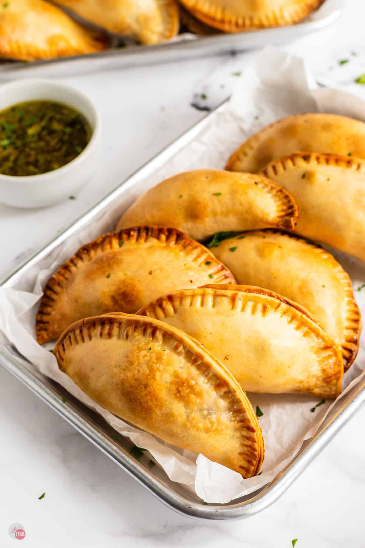 tray of beef empanadas with a small bowl of sauce next to it