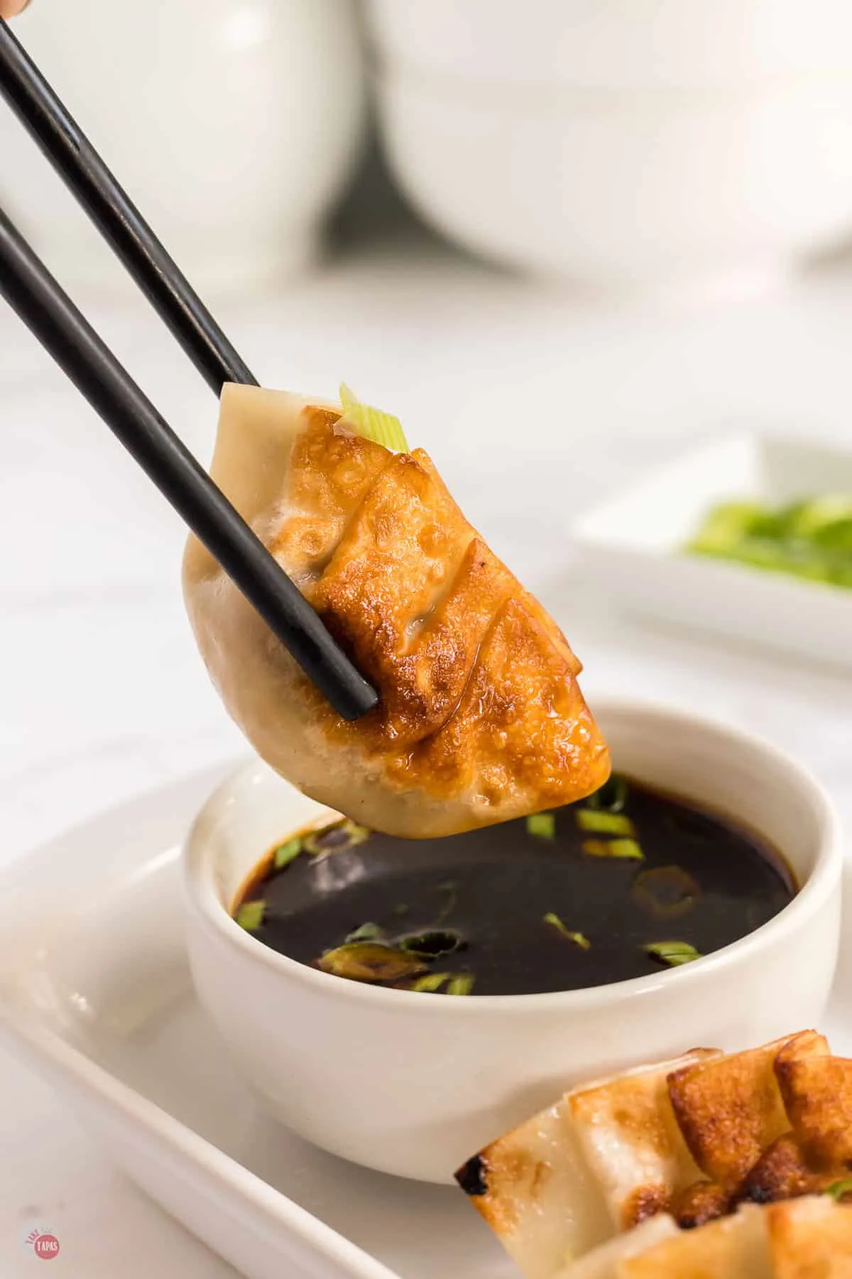 chopsticks holding gyoza over bowl of sauce