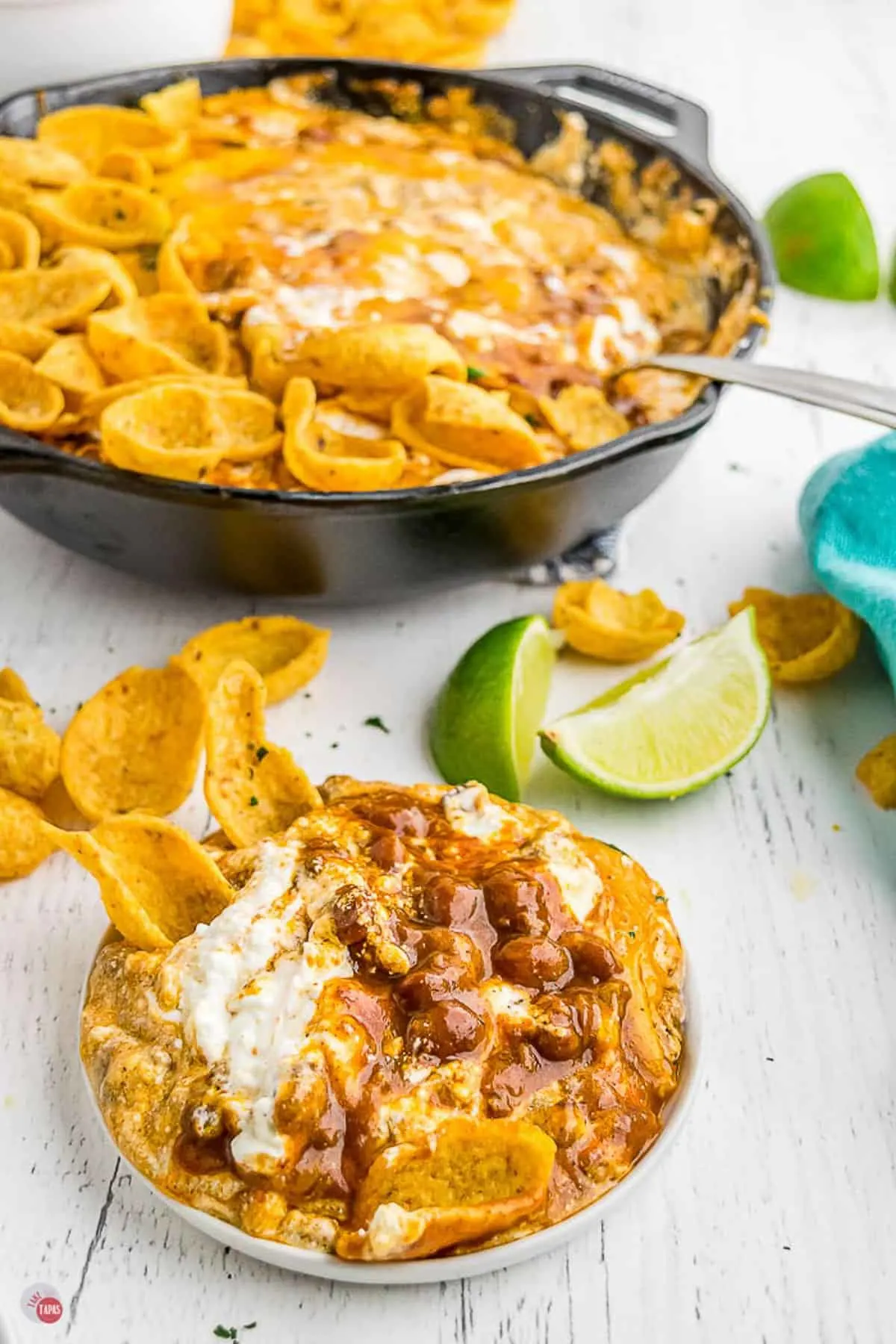 white bowl of easy frito pie dip in a white bowl with limes in the background