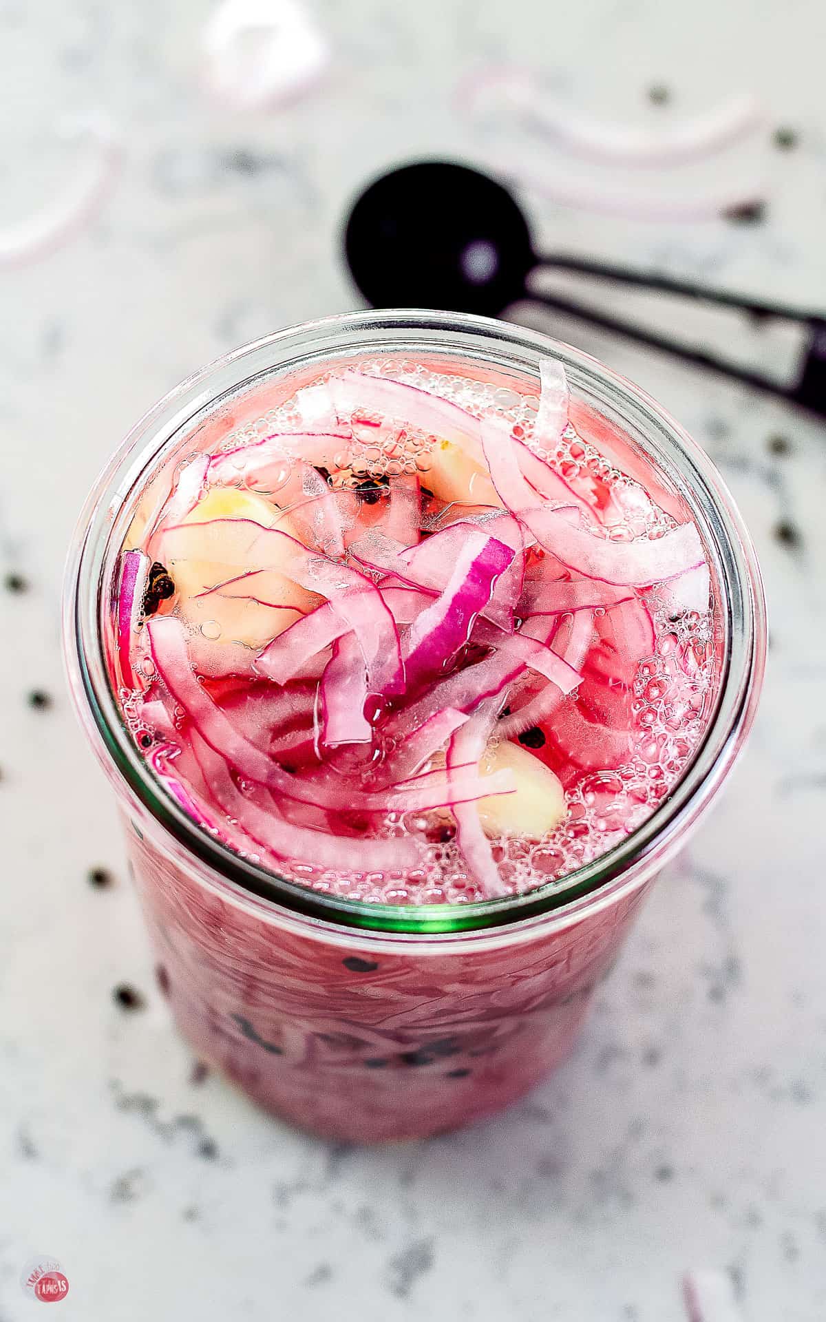 red onions in a jar with a black measuring spoon in the background