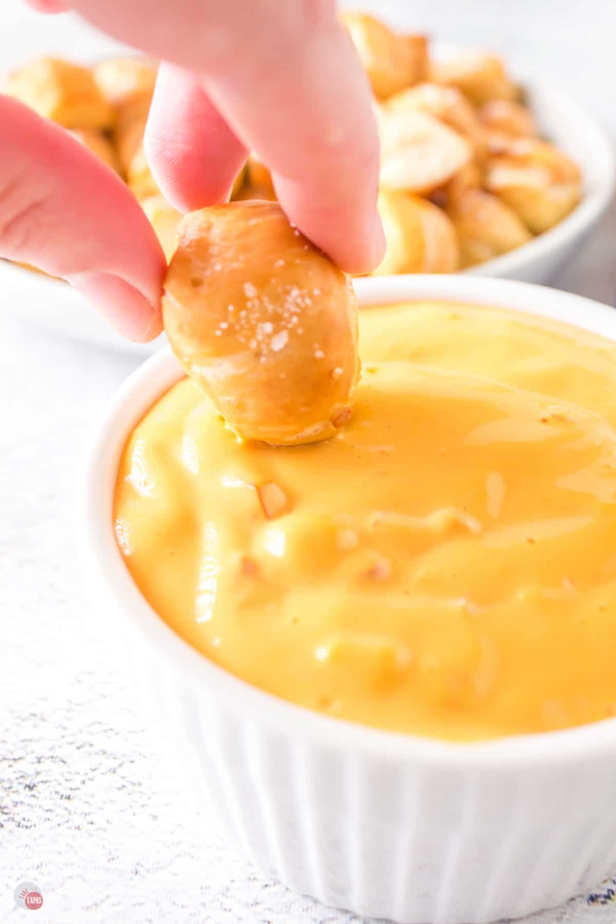 hand dipping pretzel in cheese