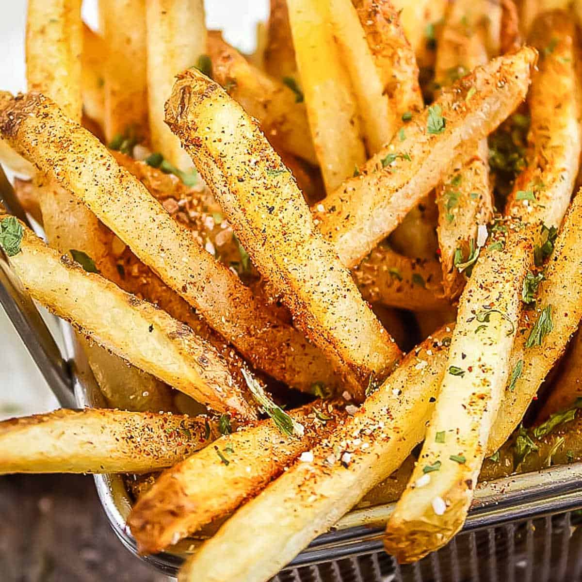 wire basket of french fries with seasoning with a napkin in the back