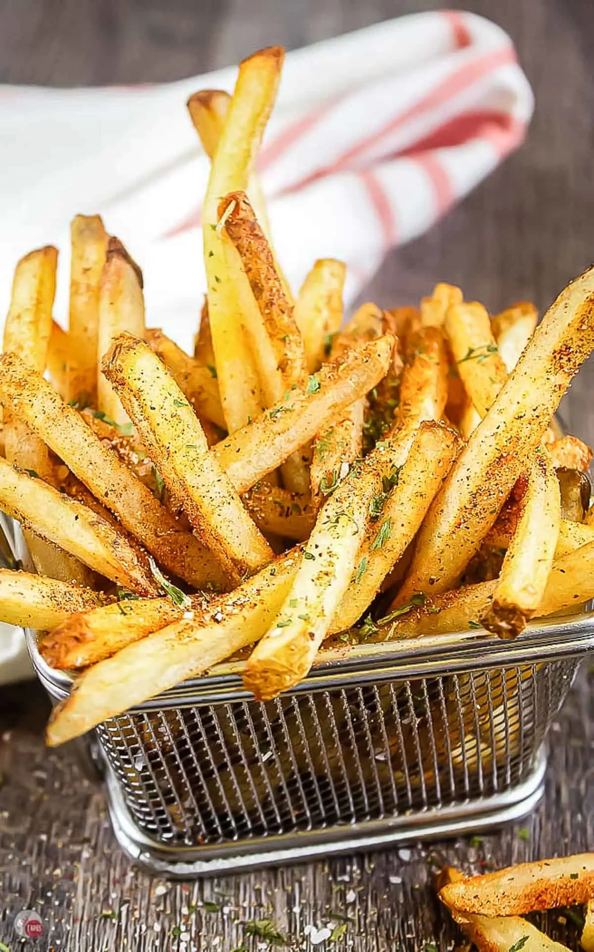 wire basket of fries with seasoning on them and a white napkin in the back