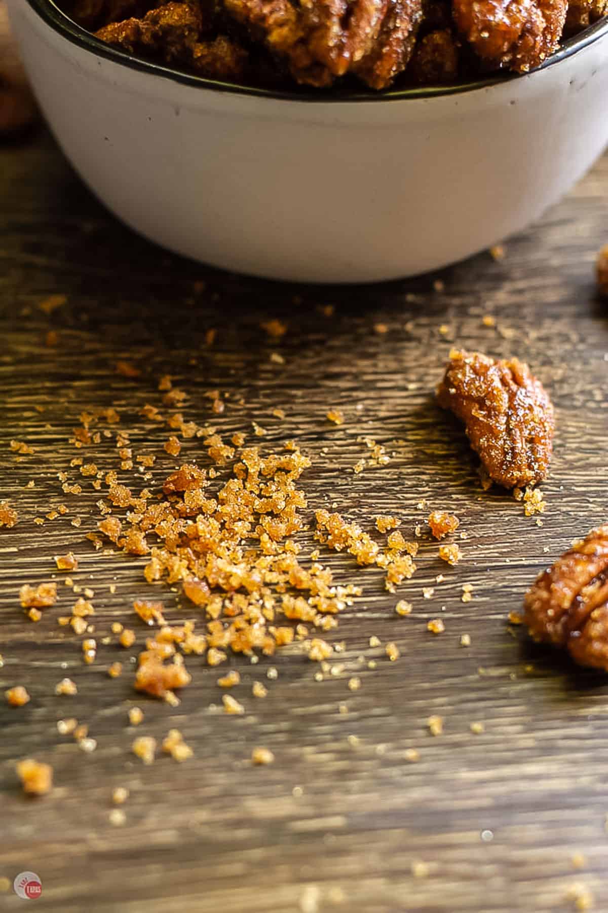 crumbs on a board next to a white bowl and scattered pecans