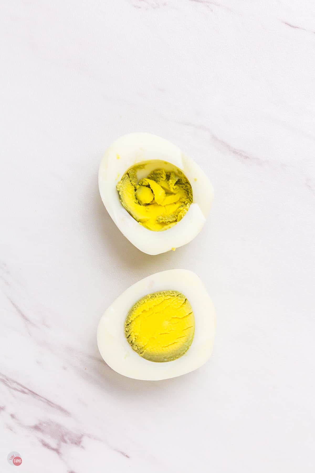 marble surface with cooked egg cut in half. The yolk is over cooked with green around the edges