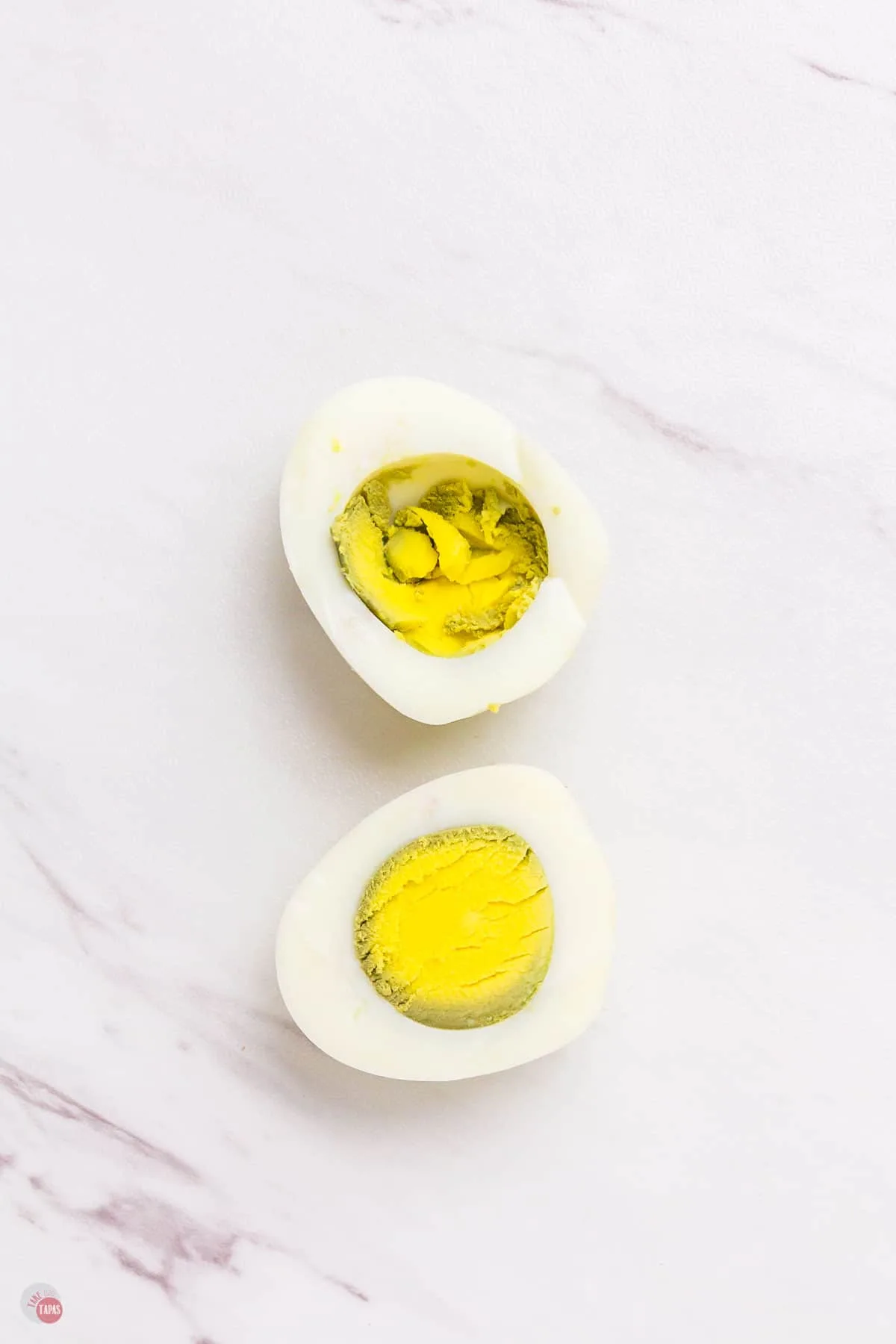 marble surface with cooked egg cut in half. The yolk is over cooked with green around the edges