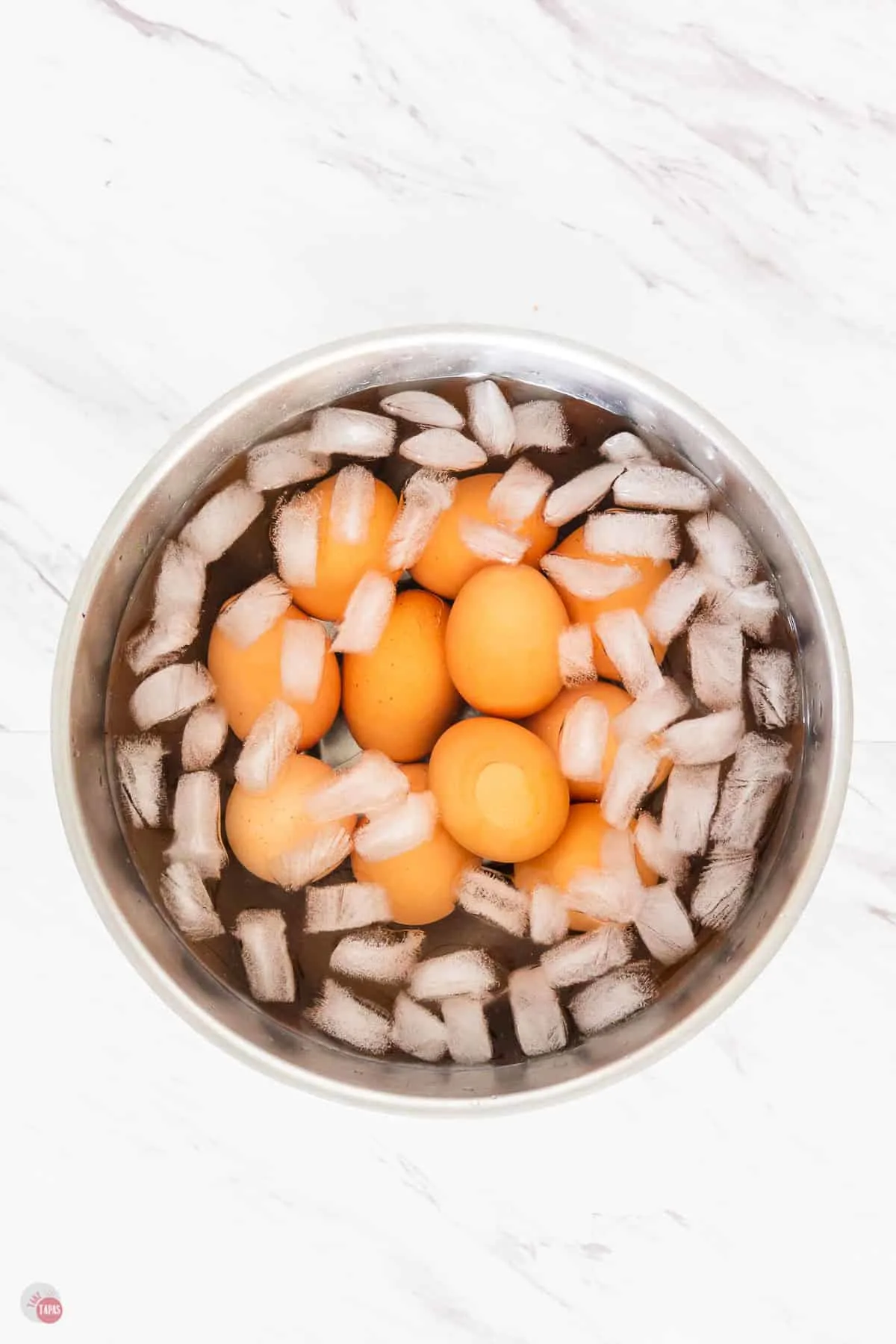 metal bowl with ice and water with brown eggs in it on a marble surface