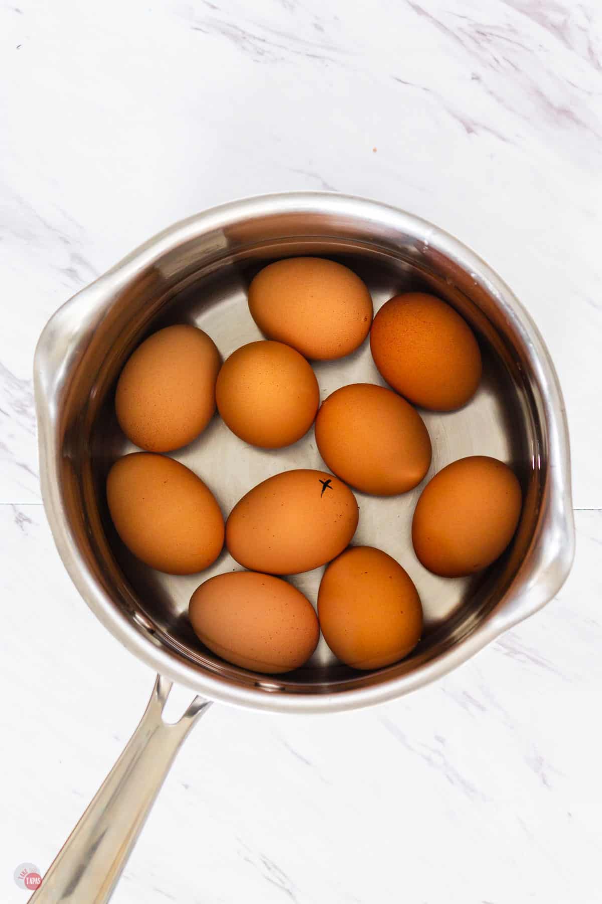 10 brown eggs in a pot of water on a marble background