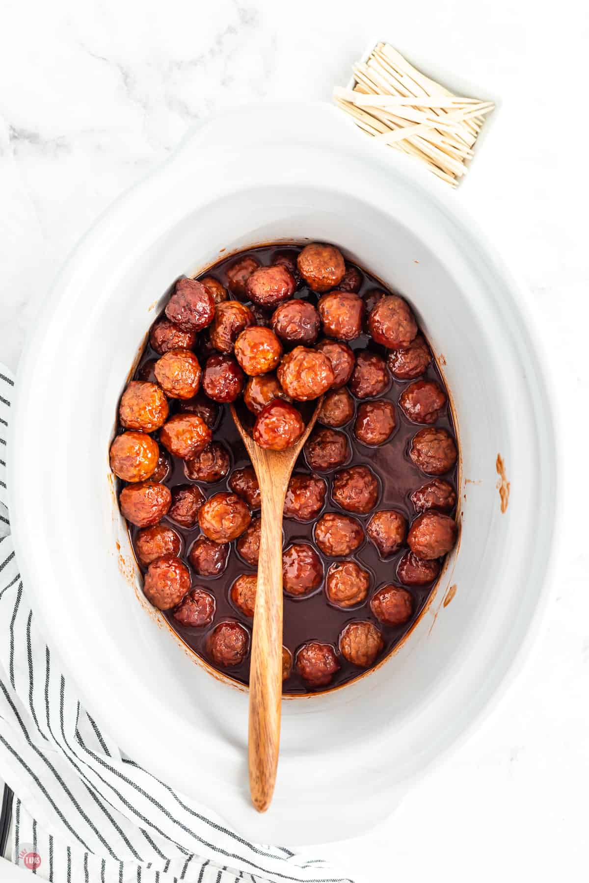 white slow cooker with meatballs, sauce, and a wood spoon