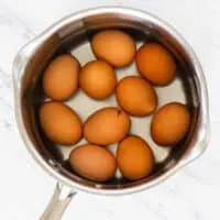 10 brown eggs in a pot with water on a marble surface