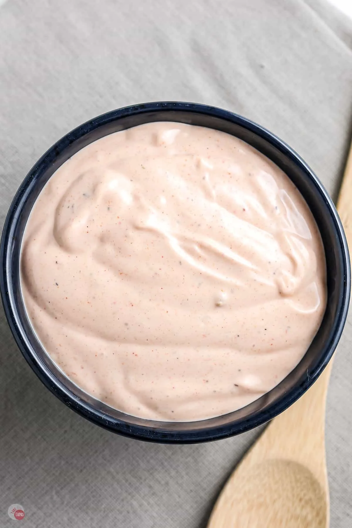 close up of small blue bowl of dipping sauce with a wood spoon next to it on a grey background