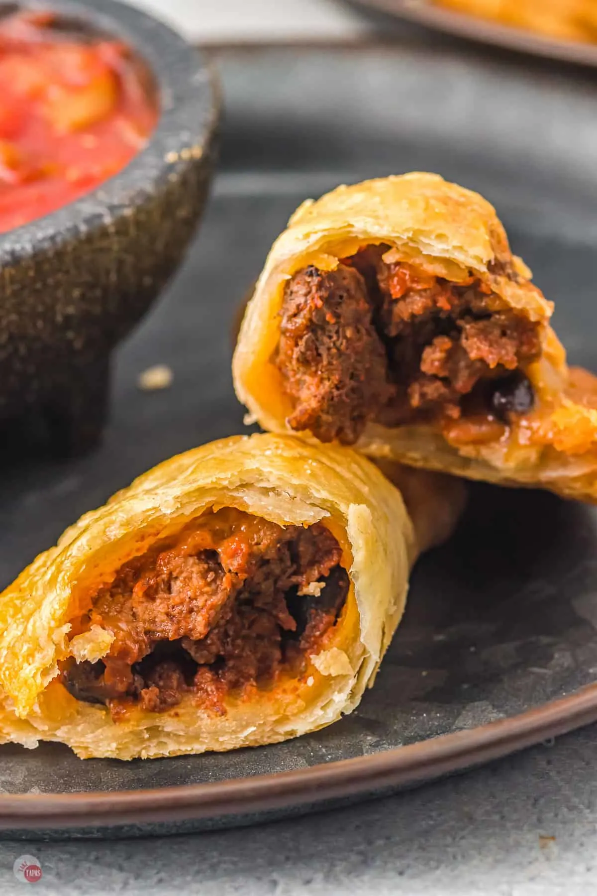 empanada broken in halg on black plate with salsa
