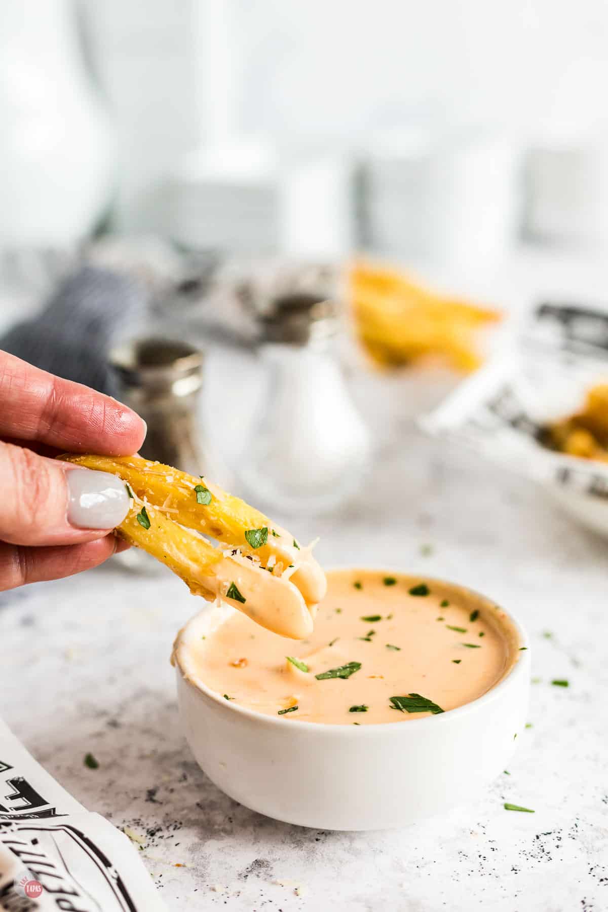 hand dipping fries in sauce
