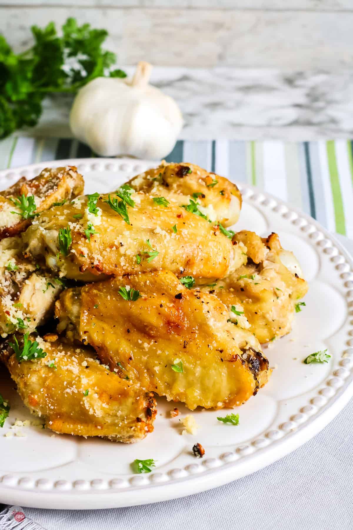 white plate with a stack of chicken wings topped with cheese and parsley