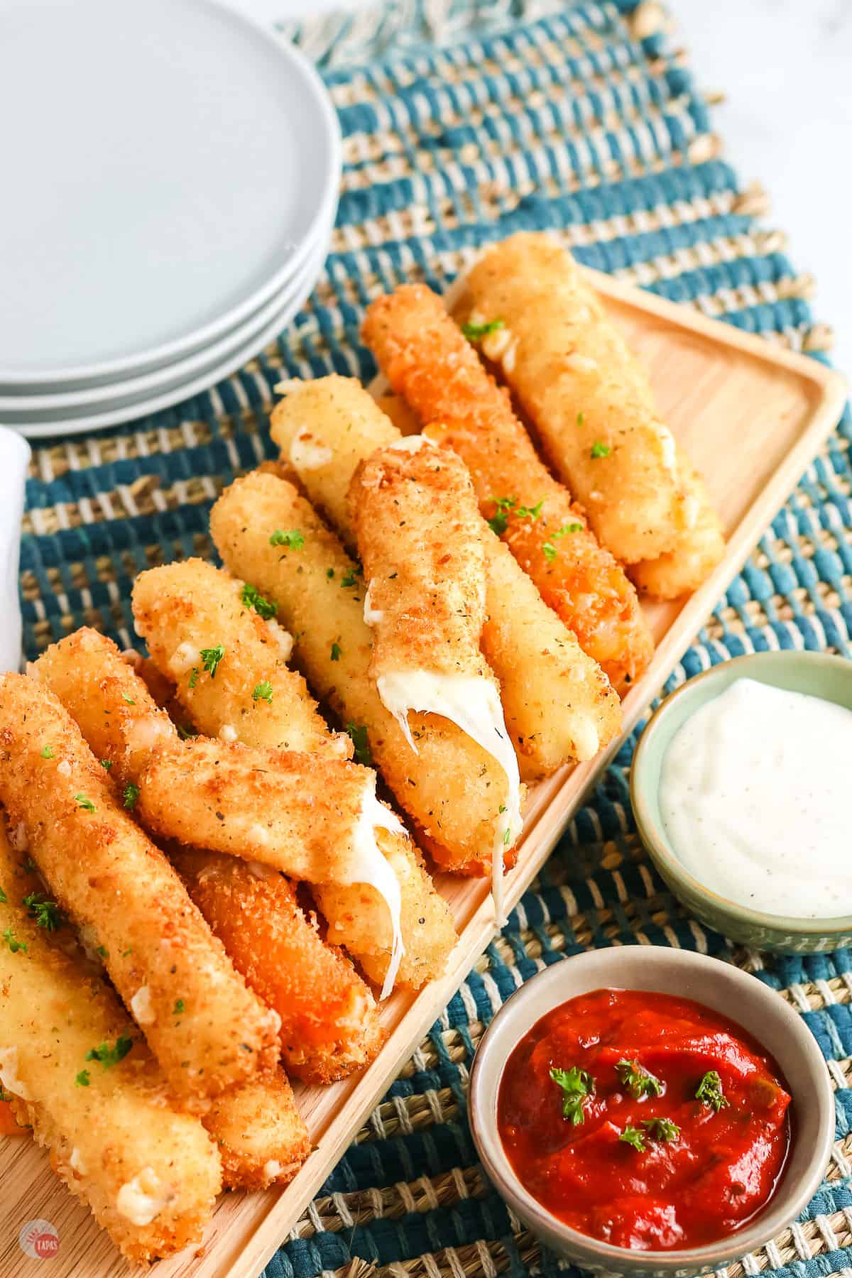 overhead picture of pile of cheese sticks with one broken in half and a small bowl of red sauce and a stack of plates