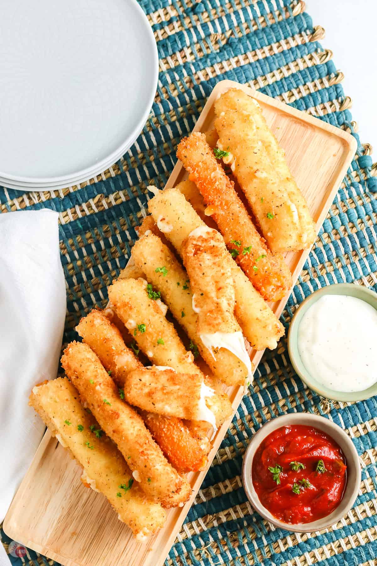 overhead picture of pile of cheese with one broken in half and a small bowl of red sauce and ranch with a stack of plates