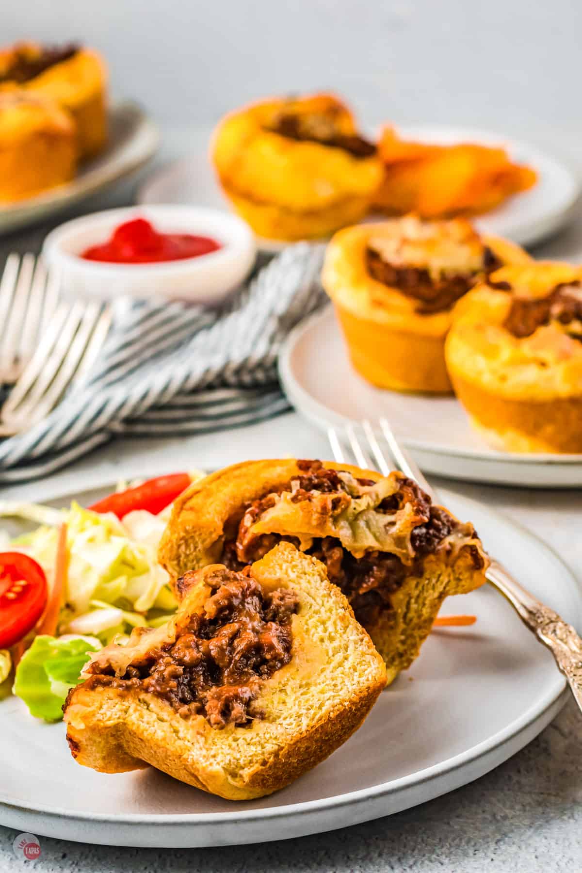 A table with a plate of Sloppy Joe Cups with some salad, with more Sloppy Joe Cups on a plate in the background.