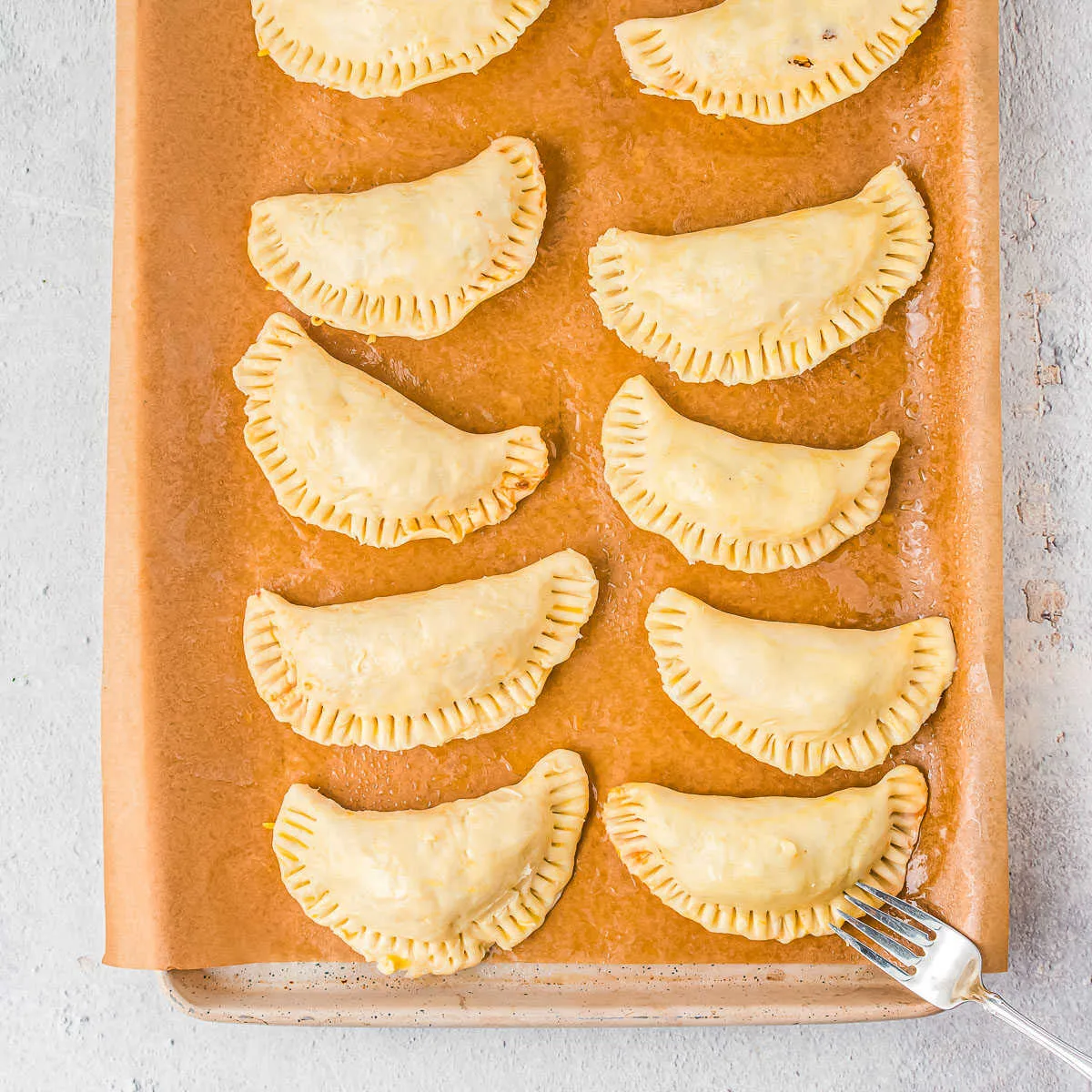 unbaked empanada dough on a baking sheet with a fork