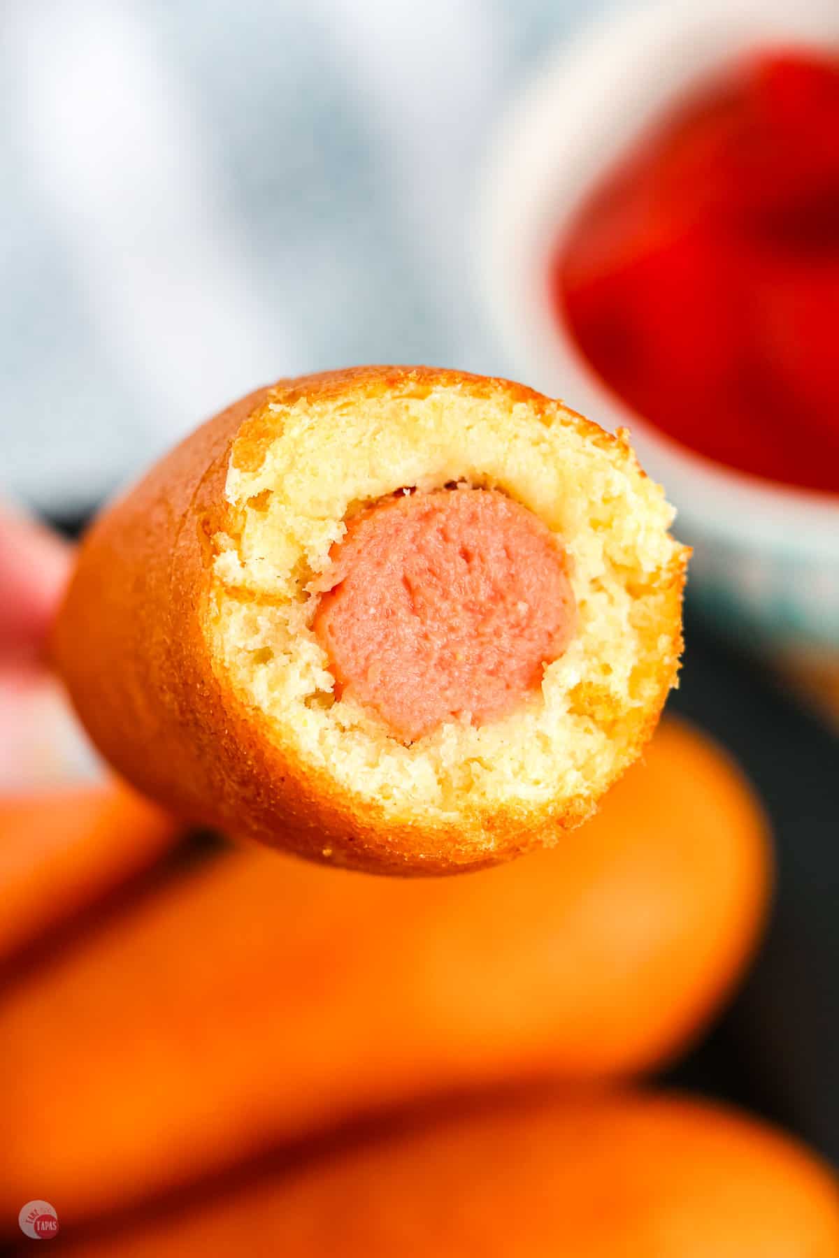 Corn dog with a bite taken off the end being held in mid-air.