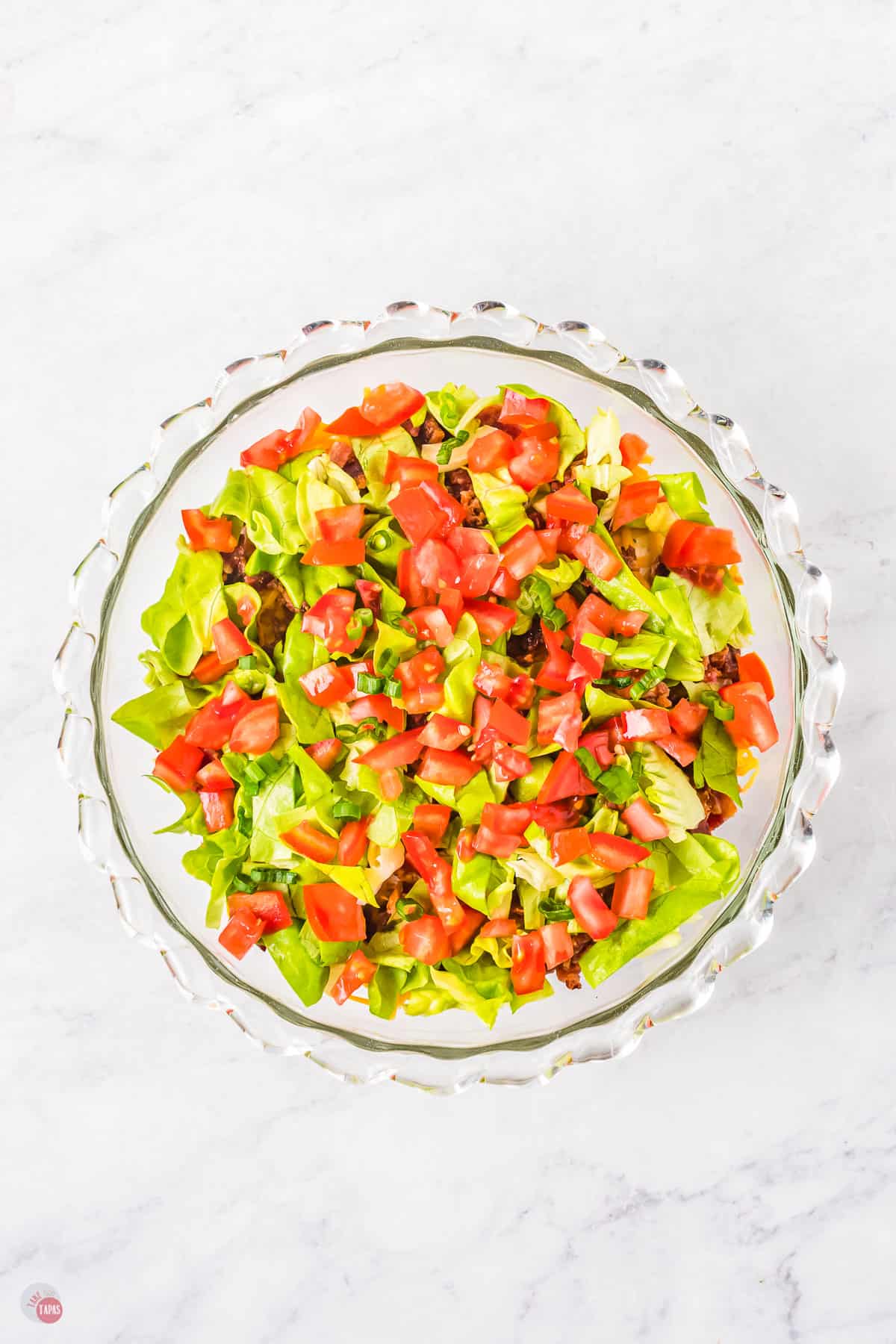 Glass bowl filled with mince with chopped tomatoes and chopped lettuce on top. 